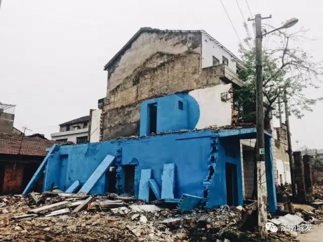 △ 這棟建筑是臨江最近的半拆遷建筑物的遺留，沅江和堤壩成為了展覽的天然背景。創(chuàng)作團(tuán)隊(duì)對(duì)這棟建筑進(jìn)行了半涂裝，將符號(hào)性的沅水曲線與拆遷進(jìn)行中的建筑立面進(jìn)行意義的疊造，它們共同觸發(fā)了場(chǎng)所空間多元語境的生成，把拆遷這種暫時(shí)破壞性、干擾性的介入行動(dòng)與沅水右岸發(fā)展的未來性、美好性緊密融合。